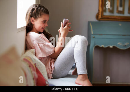 Smiling Girl Sitting on siège de fenêtre de cartes sur téléphone mobile Banque D'Images