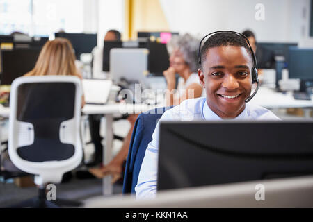 Jeune homme travaillant à l'ordinateur avec casque de bureau actif Banque D'Images