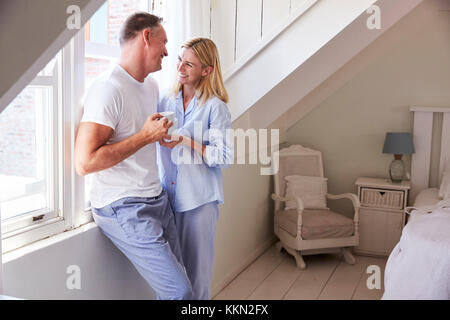 Mature Couple debout près de la fenêtre de la Chambre avec boisson chaude Banque D'Images