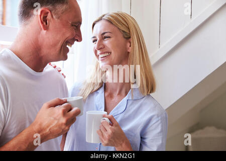 Mature Couple debout près de la fenêtre de la Chambre avec boisson chaude Banque D'Images