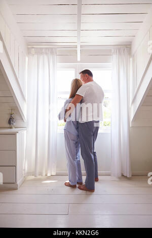 Vue arrière du Affectionate Couple debout près de la fenêtre de la chambre Banque D'Images