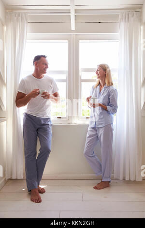 Mature Couple debout près de la fenêtre de la Chambre avec boisson chaude Banque D'Images