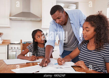 Père aide deux filles assis à table à faire leurs devoirs Banque D'Images