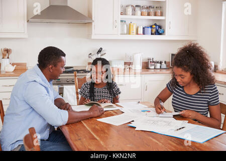 Père aide deux filles assis à table à faire leurs devoirs Banque D'Images