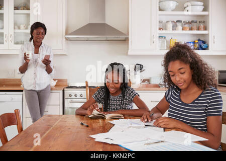 Mère utilise le téléphone comme filles autour de la table, à faire leurs devoirs Banque D'Images