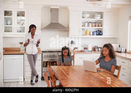 Mère utilise le téléphone comme filles autour de la table, à faire leurs devoirs Banque D'Images