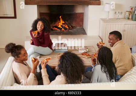 Family Sitting on sofa dans le salon à côté d'ouvrir le feu Eating Pizza Banque D'Images