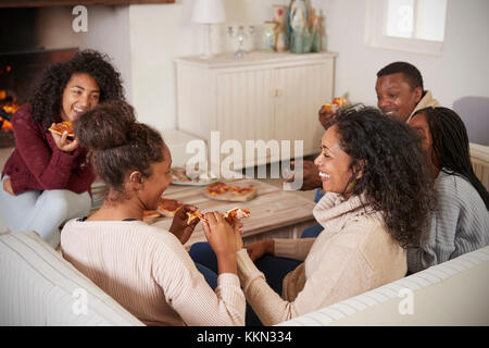 Family Sitting on sofa dans le salon à côté d'ouvrir le feu Eating Pizza Banque D'Images