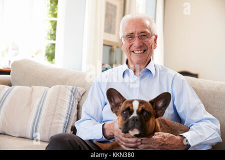 Senior Man Sitting on Sofa At Home With Pet Bouledogue Français Banque D'Images