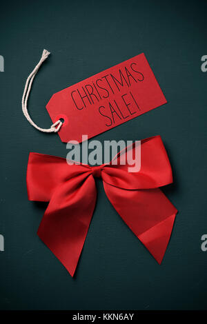 Vente de Noël le texte écrit dans un papier rouge et une étiquette de satin rouge, contre un fond vert sombre Banque D'Images