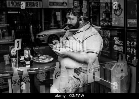 Homme mange le petit-déjeuner pendant l'utilisation de téléphone dans le centre-ville de Manchester, Angleterre, RU Banque D'Images