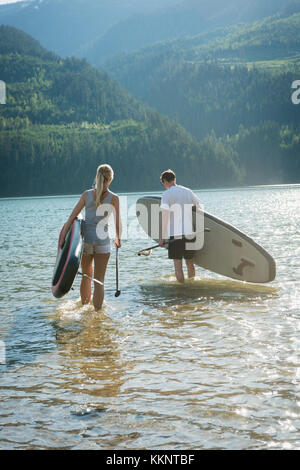 Couple avec stand up paddleboard walking in river Banque D'Images