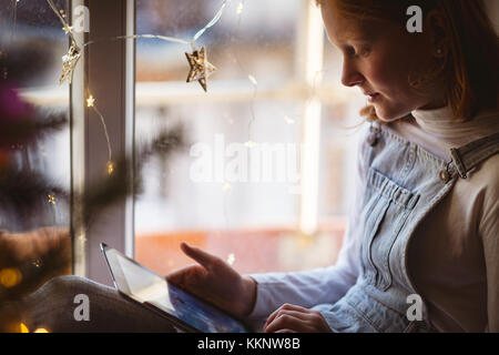 Fille assise près de la fenêtre et using digital tablet