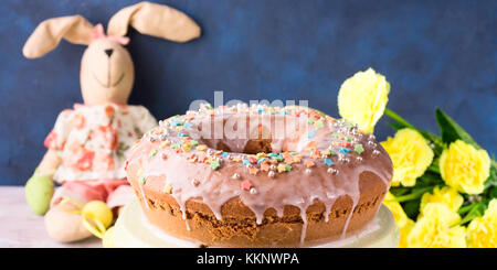 Bundt cake avec anneau de pâques glaçage sucre oeufs décorations sprinkles et poupée bunny sur fond bleu foncé. fait maison de vacances festives traiter Banque D'Images