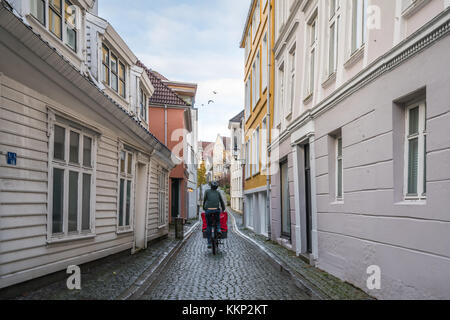 Bergen, Norvège - octobre 2017 : Homme livrant de la nourriture à vélo sur les rues étroites en galets entre les vieilles maisons traditionnelles blanches de l'ancienne Banque D'Images