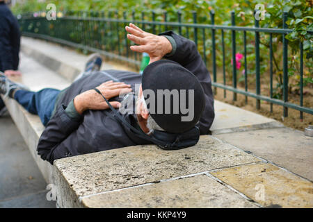 Un homme plus âgé avec un béret noir allongé sur un banc en pierre dans un parc à Paris, France Banque D'Images