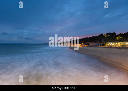 Vue crépusculaire depuis Boscombe Pier en direction de Bournemouth, Dorset, Royaume-Uni. Des vagues douces sont visibles se déplaçant vers et depuis le rivage. Banque D'Images