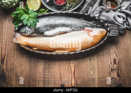 Deux poissons truite dans le plat de cuisson avec des ingrédients sur fond de bois rustique, vue du dessus, la cuisine préparation Banque D'Images