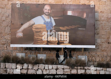 Les juifs orthodoxes en passant par une immense photographie montrant un Palestinien baker placés le long de la mur ottomane à l'extrémité ouest de la vieille ville de Jérusalem Israël Banque D'Images