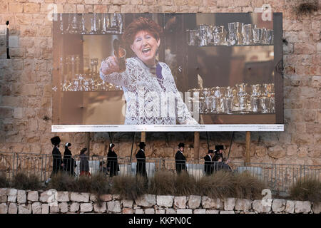 Un groupe de Juifs orthodoxes en passant par une immense photographie représentant un artiste juif Judaica placés le long de la mur ottomane à l'extrémité ouest de la vieille ville de Jérusalem Israël Banque D'Images