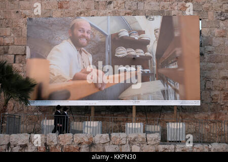 Les juifs orthodoxes en passant par une immense photographie représentant un Juif juif traditionnel tissage Talitot placés le long de la mur ottomane à l'extrémité ouest de la vieille ville de Jérusalem Israël Banque D'Images