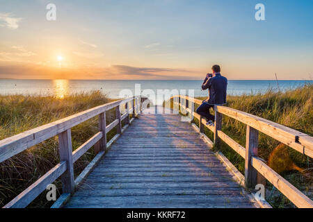 Weissenhäuser Strand, Ostholstein, Schleswig-Holstein, Allemagne. Man photographing le coucher du soleil sur une jetée à la mer Baltique. Banque D'Images