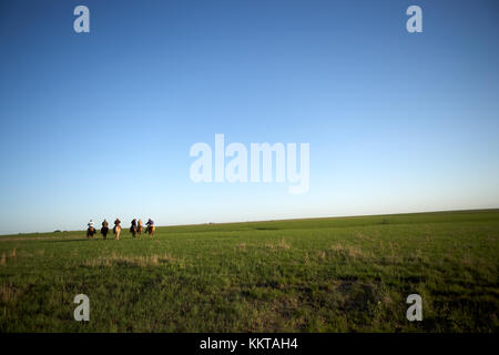 Groupe de cowboys à cheval vue à une distance équitation sur une large gamme ouverte avec l'herbe verte au coucher du soleil avec une vignette Banque D'Images