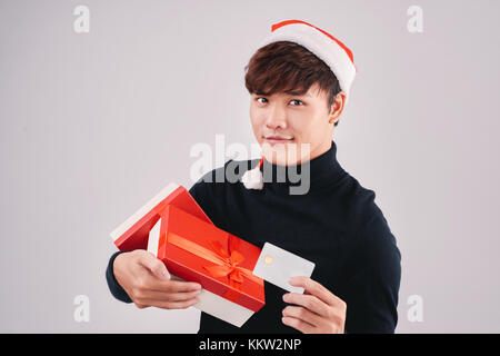 Young attractive asian man in santa claus hat holding boîte cadeau et carte de crédit Banque D'Images