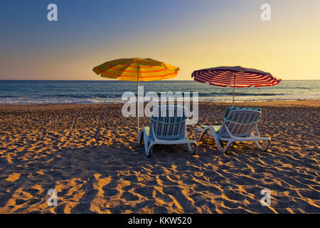 Deux chaises vides sous des parasols sur une plage de sable à l'heure d'été Banque D'Images