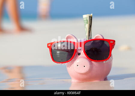 Moneybox de porc rose en lunettes de soleil rouges sur la plage Banque D'Images