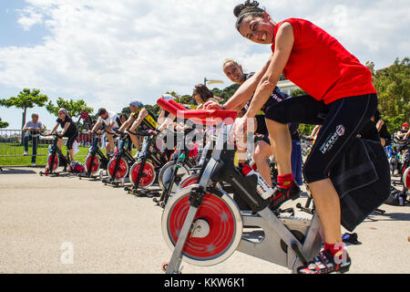 Les gens qui sont à cheval sur un vélo d'exercice dans un parc urbain à Imperia. -----Imperia, IM, Italie - 18 mai 2014 : Les gens d'effectuer une session de spinning Banque D'Images