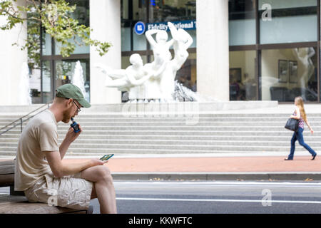 Portland, Oregon, USA - Septembre 9th, 2017 : un homme est assis fumer une cigarette électronique et à son portable dans la rue à Seattle. Banque D'Images