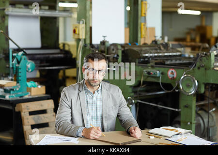 Ingénieur sérieux avec le bloc-notes et crayon à dessiner par son lieu de travail en usine Banque D'Images