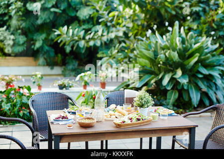 Table avec de la nourriture maison préparée pour les amis se réunissant avec des fauteuils en osier autour dans le jardin Banque D'Images