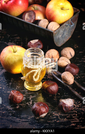 Pot de miel en verre avec les pommes, les châtaignes et les noix de table en bois noir Banque D'Images