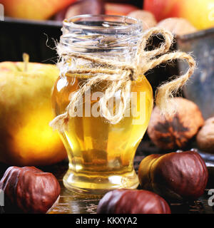 Pot de miel en verre avec les pommes, les châtaignes et les noix de table en bois noir carré. image. Banque D'Images