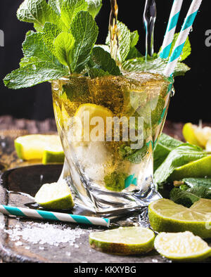 Verre de mojito cocktail Rhum avec bec verseur et le soda, la menthe fraîche, des limes et des cubes de glace sur fond noir. Banque D'Images