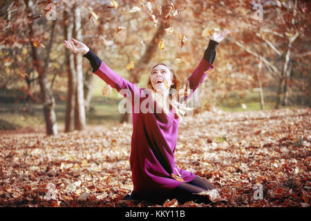 Jeune femme dans un beau parc d'automne, concept de l'automne. fille, assis dans les bois, feuilles jette en l'air et sourit. Banque D'Images