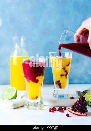 Verser la grenadine dans deux verres de boissons cocktail avec de la liqueur d'orange, jus d'ananas et du jus de grenade et de la chaux et de la glace sur le Banque D'Images