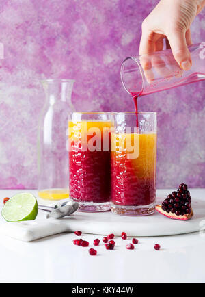 Verser la grenadine dans deux verres de boissons cocktail avec de la liqueur d'orange, jus d'ananas et du jus de grenade et de la chaux et de la glace sur le Banque D'Images