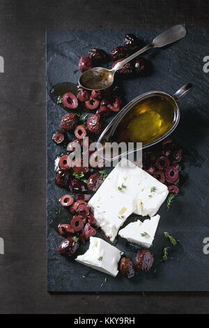 Ensemble et olives noires et le bloc de fromage feta à l'huile d'olive sur l'ardoise noire sur fond sombre vue de dessus. Banque D'Images