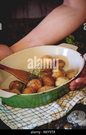 Woman's hands prendre metal avec pan fried jeunes pommes de terre et de l'aneth frais. sur table en bois noir à carreaux avec des essuie-tout. dark style rustique. natura Banque D'Images