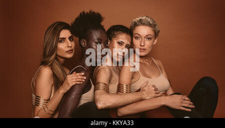 Portrait de femme avec différents modèles d'habillages. Groupe de jeunes femmes siégeant ensemble et à la recherche à l'appareil photo sur fond brun. Banque D'Images