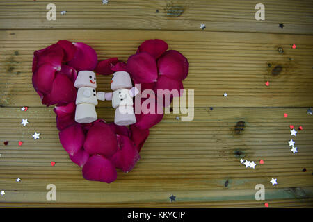 La photographie d'hiver romantique avec des pétales de rose rouge et des coeurs dans l'amour avec de la nourriture de forme en forme de bonhomme que les guimauves sur un fond de bois rustique Banque D'Images