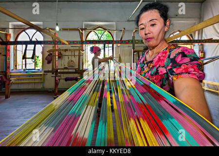 Les femmes travaillent et tissent des étoffes en soie dans l'usine de soie Yodgorlik traditionnels, dans Marguilan, Ouzbékistan. Banque D'Images