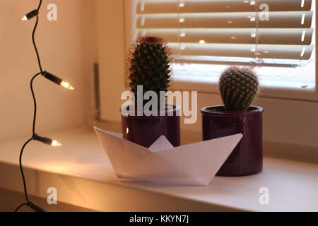 Les lumières de Noël cactus et un bateau de papier sur une décoration de fenêtre d'accueil Banque D'Images