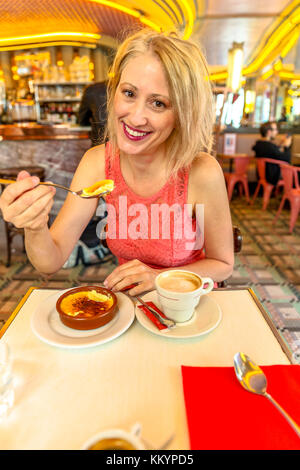 Une femme élégante et heureuse mange des crèmes de son français ou des crèmes de crème brûlée au capuccino. Voyage style de vie touristique dans le café-brasserie populaire de Montmartre, Paris. Banque D'Images