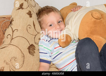 Portrait de petit garçon aux cheveux juste jouer avec la pâte à modeler et l'ours accueil sur le canapé Banque D'Images