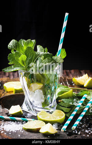 Ingrédients pour le mojito (menthe, citron vert, glace, sucre) en verre avec cocktail rétro sur noir. Banque D'Images