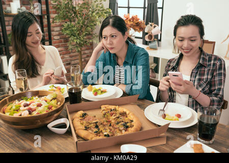 Belle jeune fille se sent malheureux son ami à l'aide jouer smart mobile phone lors de dîner à la maison. Banque D'Images